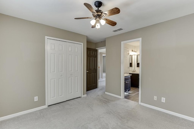 unfurnished bedroom with ceiling fan, ensuite bath, light colored carpet, and a closet