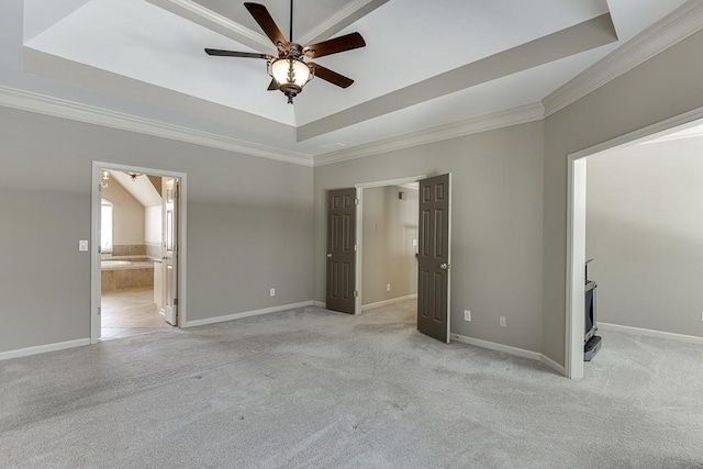 unfurnished bedroom with ceiling fan, ensuite bathroom, a tray ceiling, and light carpet