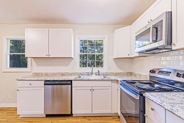 kitchen featuring appliances with stainless steel finishes, light hardwood / wood-style floors, white cabinetry, and a wealth of natural light