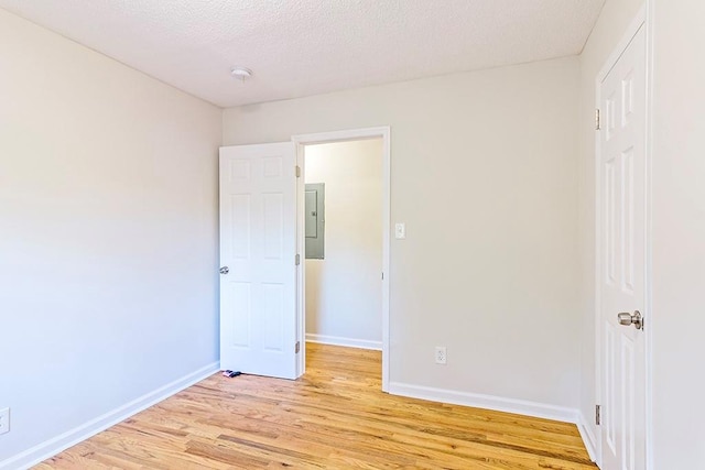 unfurnished bedroom featuring electric panel, light hardwood / wood-style flooring, and a textured ceiling