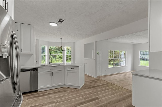 1069 Alford Rd, Lithonia, GA 30058 - kitchen featuring stainless steel appliances, a textured ceiling, a peninsula, white cabinetry, and light wood-style floors