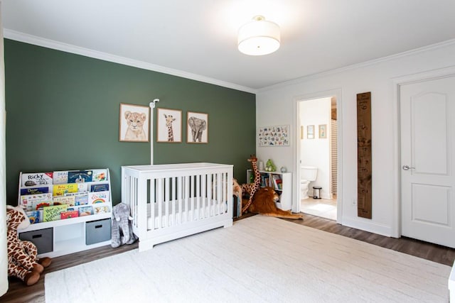 bedroom with baseboards, ensuite bath, ornamental molding, wood finished floors, and a nursery area