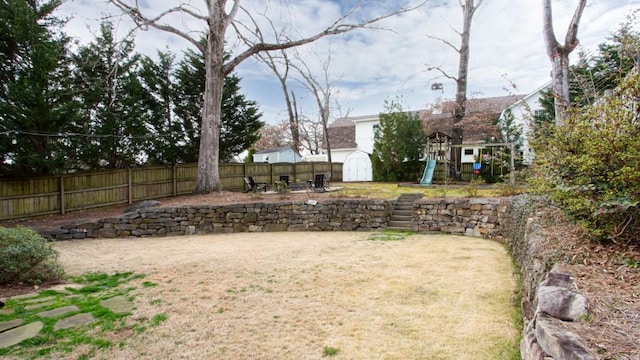 view of yard featuring a storage shed, an outdoor structure, fence, and a playground