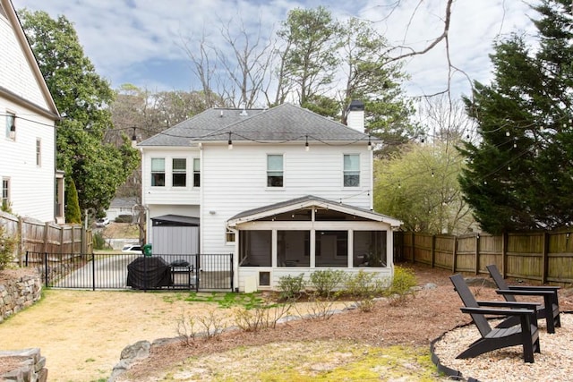 back of property with an outdoor fire pit, a sunroom, a fenced backyard, a chimney, and roof with shingles