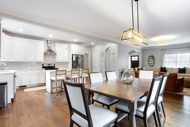 dining room with recessed lighting, arched walkways, wood finished floors, and ornamental molding