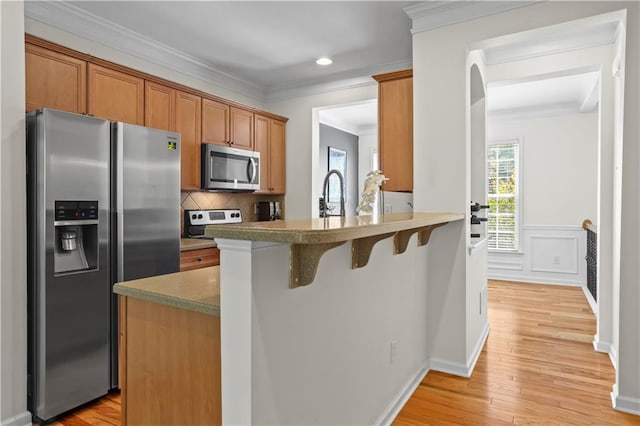 kitchen with a sink, appliances with stainless steel finishes, a kitchen breakfast bar, brown cabinets, and decorative backsplash