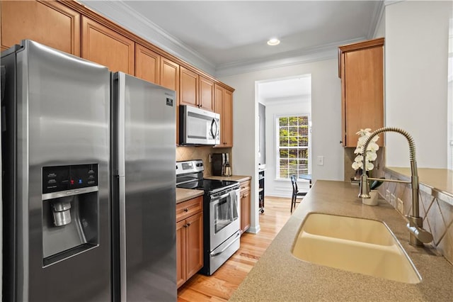 kitchen featuring tasteful backsplash, ornamental molding, stainless steel appliances, light wood finished floors, and a sink