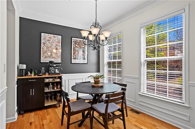dining area featuring light wood-type flooring, ornamental molding, a chandelier, a wainscoted wall, and visible vents