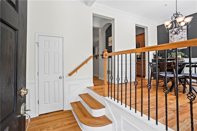 stairway featuring crown molding, wood finished floors, a notable chandelier, and arched walkways