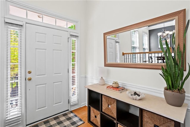 entrance foyer featuring light wood-style floors, a notable chandelier, and a wainscoted wall