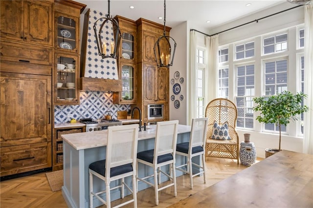 11277 Serenbe Ln, Chattahoochee Hills, GA 30268 - kitchen with light countertops, brown cabinets, backsplash, pendant lighting, and an island with sink