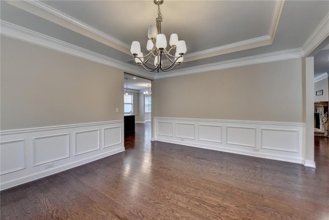 spare room with ornamental molding, dark wood-type flooring, a raised ceiling, a wainscoted wall, and a notable chandelier