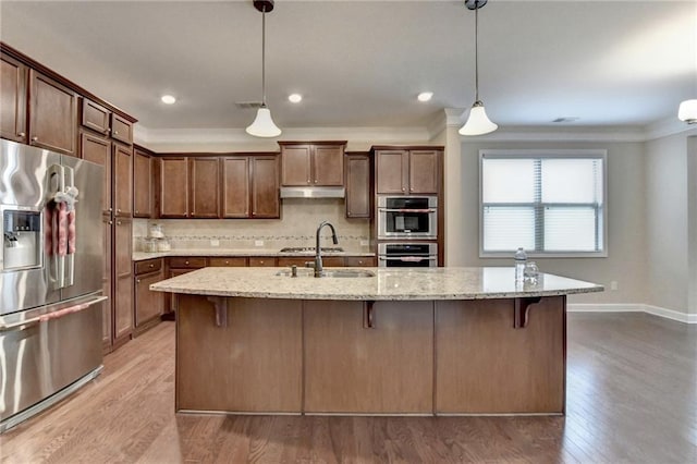 kitchen with light stone counters, light wood-style floors, stainless steel appliances, backsplash, and under cabinet range hood