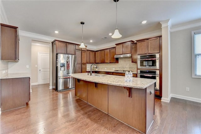 kitchen with ornamental molding, under cabinet range hood, a sink, backsplash, and stainless steel appliances
