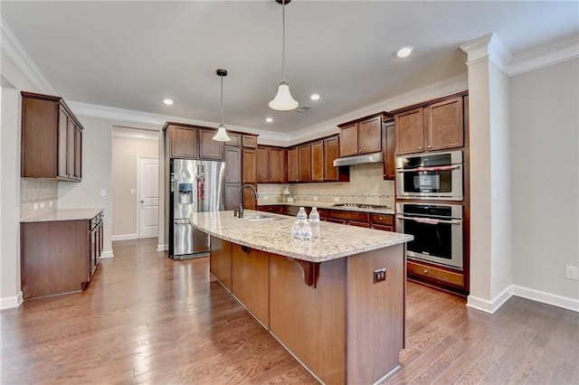 kitchen with light stone countertops, stainless steel appliances, backsplash, under cabinet range hood, and ornamental molding