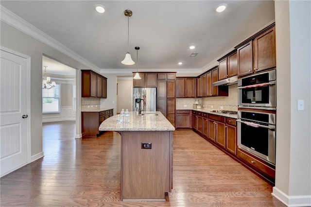 kitchen with a kitchen island with sink, light wood-style flooring, stainless steel appliances, backsplash, and under cabinet range hood