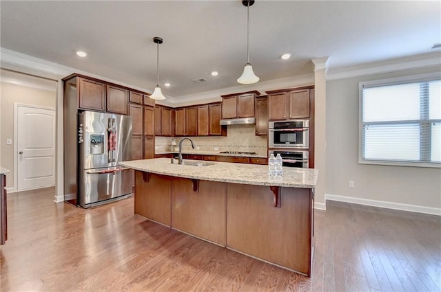 kitchen with crown molding, under cabinet range hood, tasteful backsplash, a sink, and appliances with stainless steel finishes