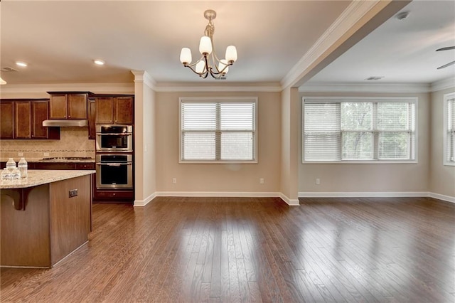 kitchen with decorative backsplash, double oven, under cabinet range hood, light stone counters, and cooktop