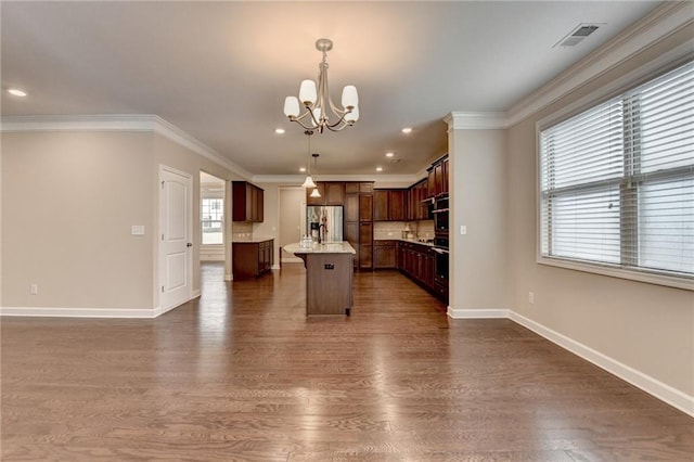 kitchen with stainless steel fridge, a chandelier, a kitchen island, visible vents, and ornamental molding