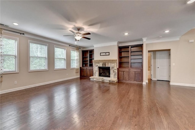unfurnished living room with ceiling fan, a stone fireplace, visible vents, baseboards, and ornamental molding