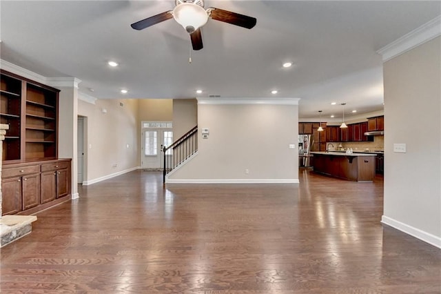 unfurnished living room with crown molding, a ceiling fan, baseboards, and stairway