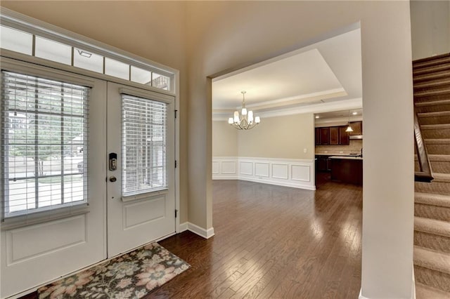 foyer entrance with an inviting chandelier, dark wood finished floors, a decorative wall, and stairway