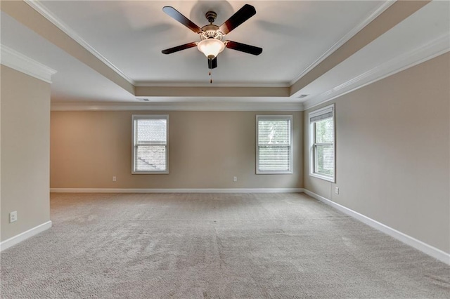 carpeted spare room featuring a ceiling fan, a tray ceiling, ornamental molding, and a healthy amount of sunlight