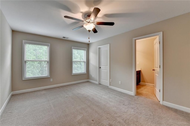 unfurnished bedroom with baseboards, light carpet, ensuite bath, and visible vents