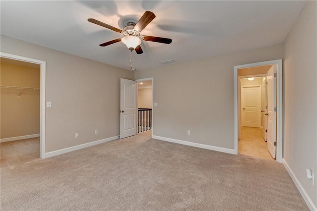 unfurnished bedroom with ensuite bathroom, a walk in closet, baseboards, and light carpet
