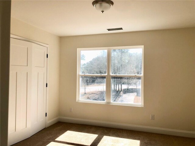 unfurnished room with carpet floors, visible vents, and baseboards