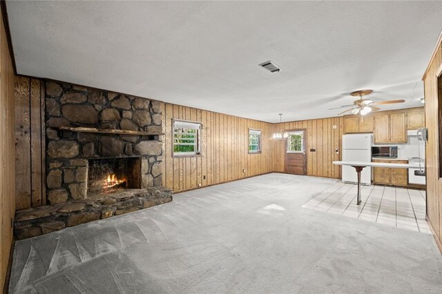 unfurnished living room featuring a fireplace, light colored carpet, wooden walls, and ceiling fan