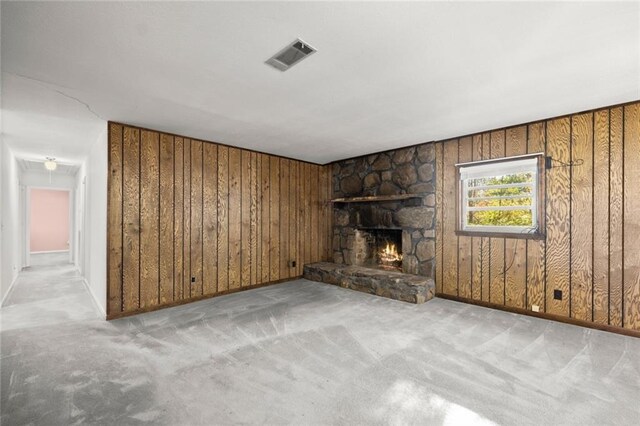 unfurnished living room with a stone fireplace, light colored carpet, and wood walls