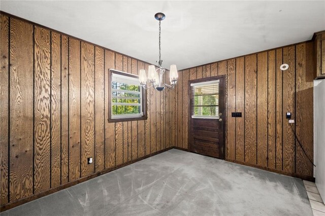 carpeted empty room with wood walls, plenty of natural light, and an inviting chandelier