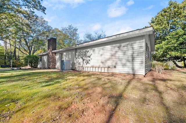 rear view of property featuring central air condition unit and a lawn