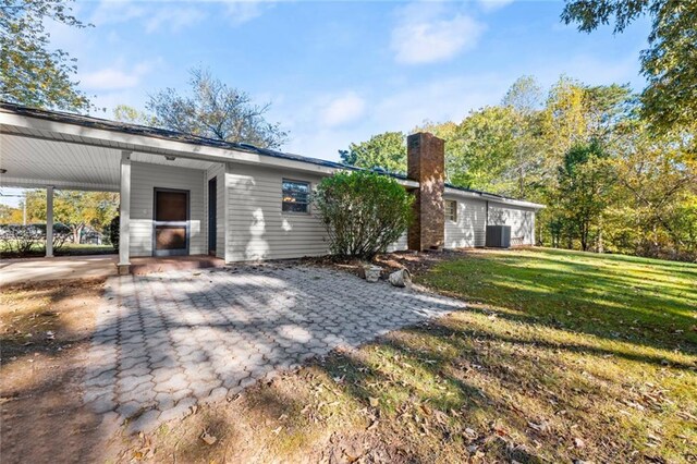 rear view of property with a lawn, cooling unit, and a carport