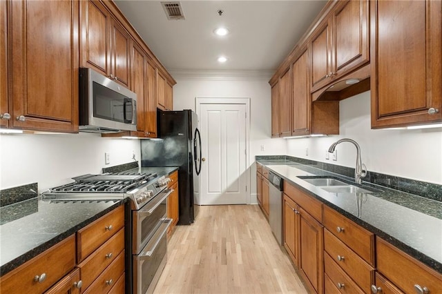 kitchen featuring sink, appliances with stainless steel finishes, dark stone countertops, ornamental molding, and light hardwood / wood-style floors