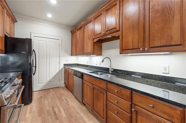 kitchen with appliances with stainless steel finishes, sink, dark stone countertops, ornamental molding, and light hardwood / wood-style floors