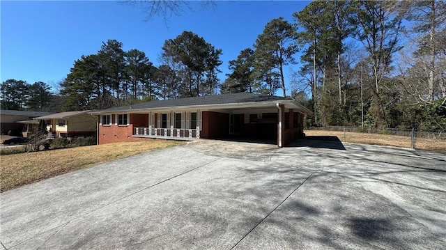 single story home with brick siding, a porch, fence, a carport, and driveway