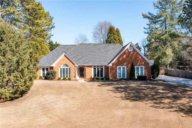 view of front of house with a shingled roof, dirt driveway, fence, and brick siding