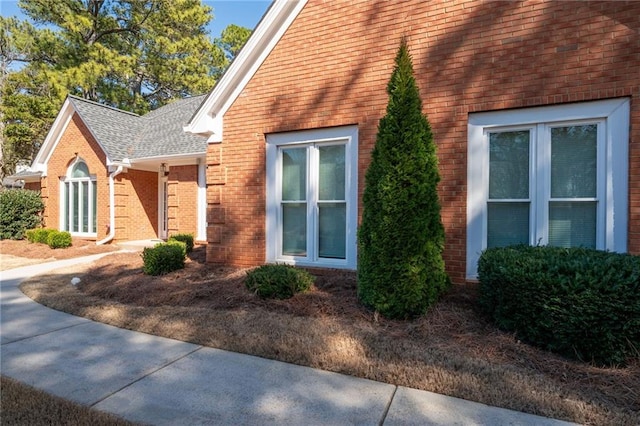 view of side of property featuring brick siding and roof with shingles