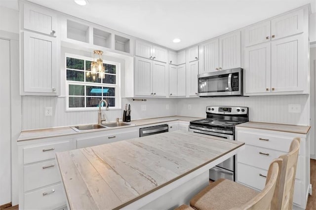 kitchen featuring stainless steel appliances, hanging light fixtures, sink, white cabinets, and a kitchen bar