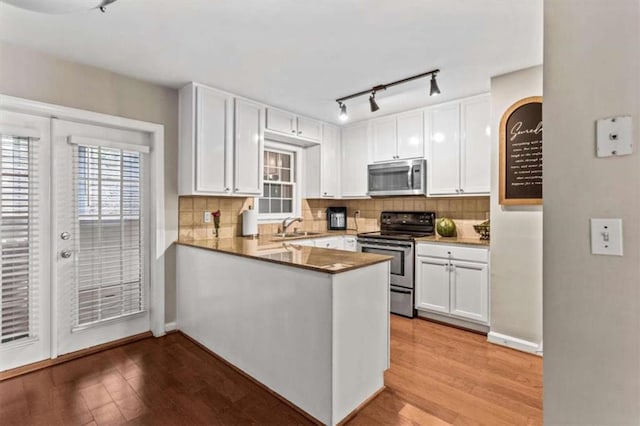 kitchen featuring appliances with stainless steel finishes, a sink, white cabinetry, track lighting, and light wood-style floors