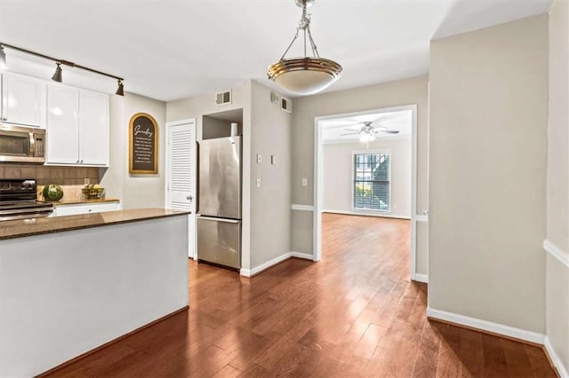 kitchen with appliances with stainless steel finishes, rail lighting, decorative backsplash, and wood finished floors