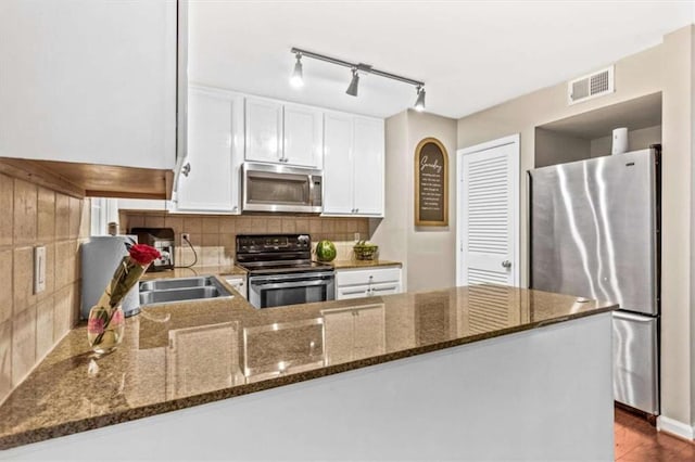 kitchen with appliances with stainless steel finishes, a peninsula, tasteful backsplash, dark stone countertops, and white cabinetry