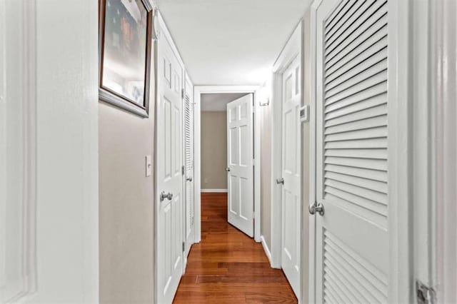 corridor with dark wood-style flooring and baseboards