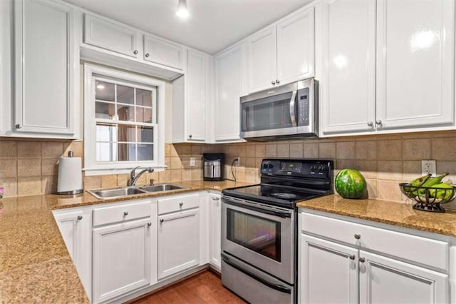 kitchen featuring stainless steel appliances, a sink, white cabinets, tasteful backsplash, and light stone counters