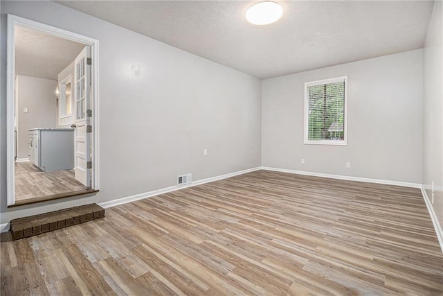 unfurnished room featuring a textured ceiling, baseboards, visible vents, and light wood-style flooring