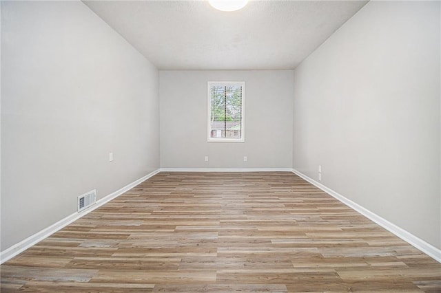 empty room featuring light wood-style floors, baseboards, and visible vents