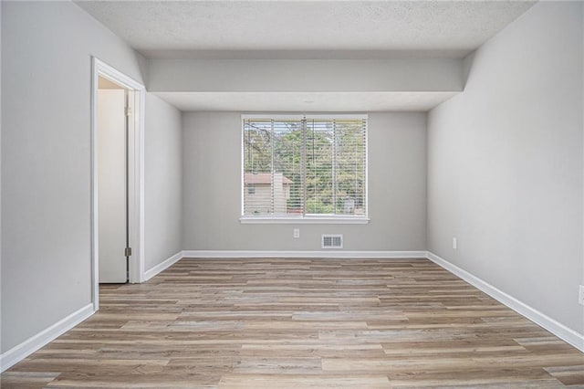 unfurnished room featuring baseboards, light wood-type flooring, a textured ceiling, and visible vents