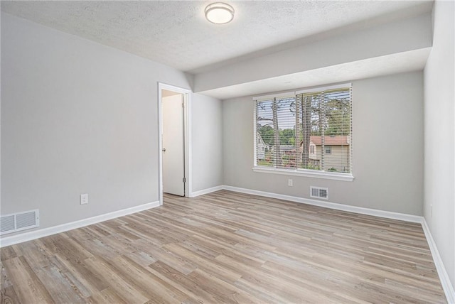 unfurnished room with light wood finished floors, a textured ceiling, and visible vents